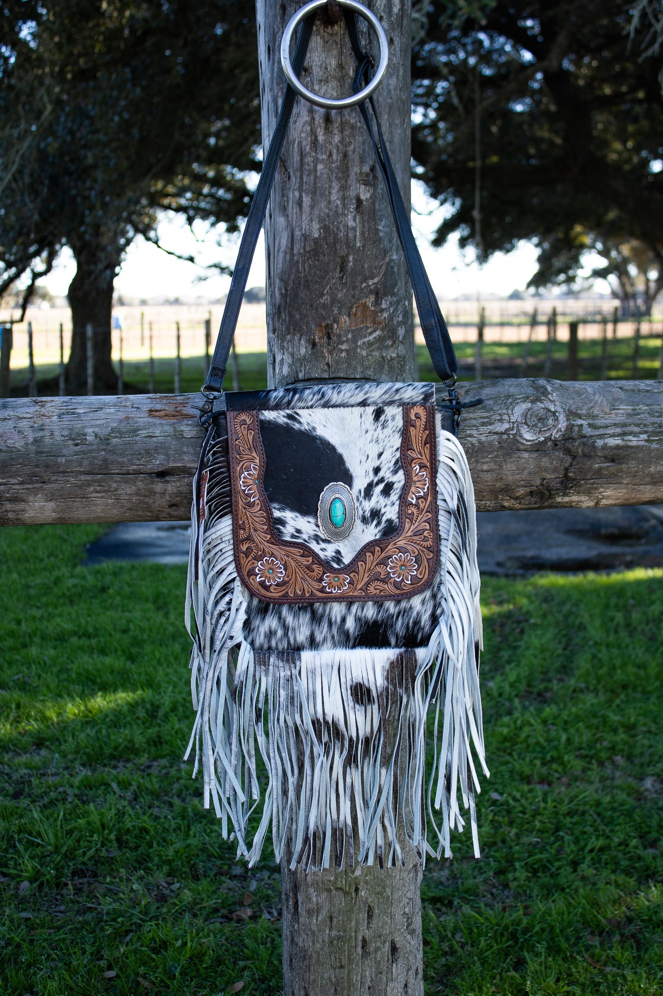 black and white cowhide purse with cowhide fringe, tooled leather and turquoise concho on front, black shoulder strap