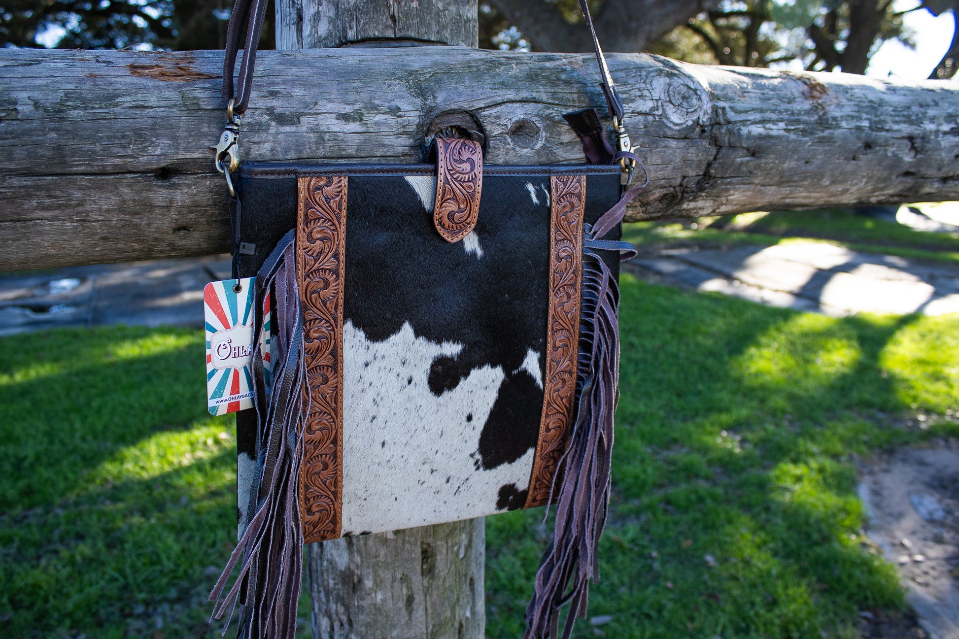 black and white cowhide purse with brown tooled leather accent and brown fringe on the side