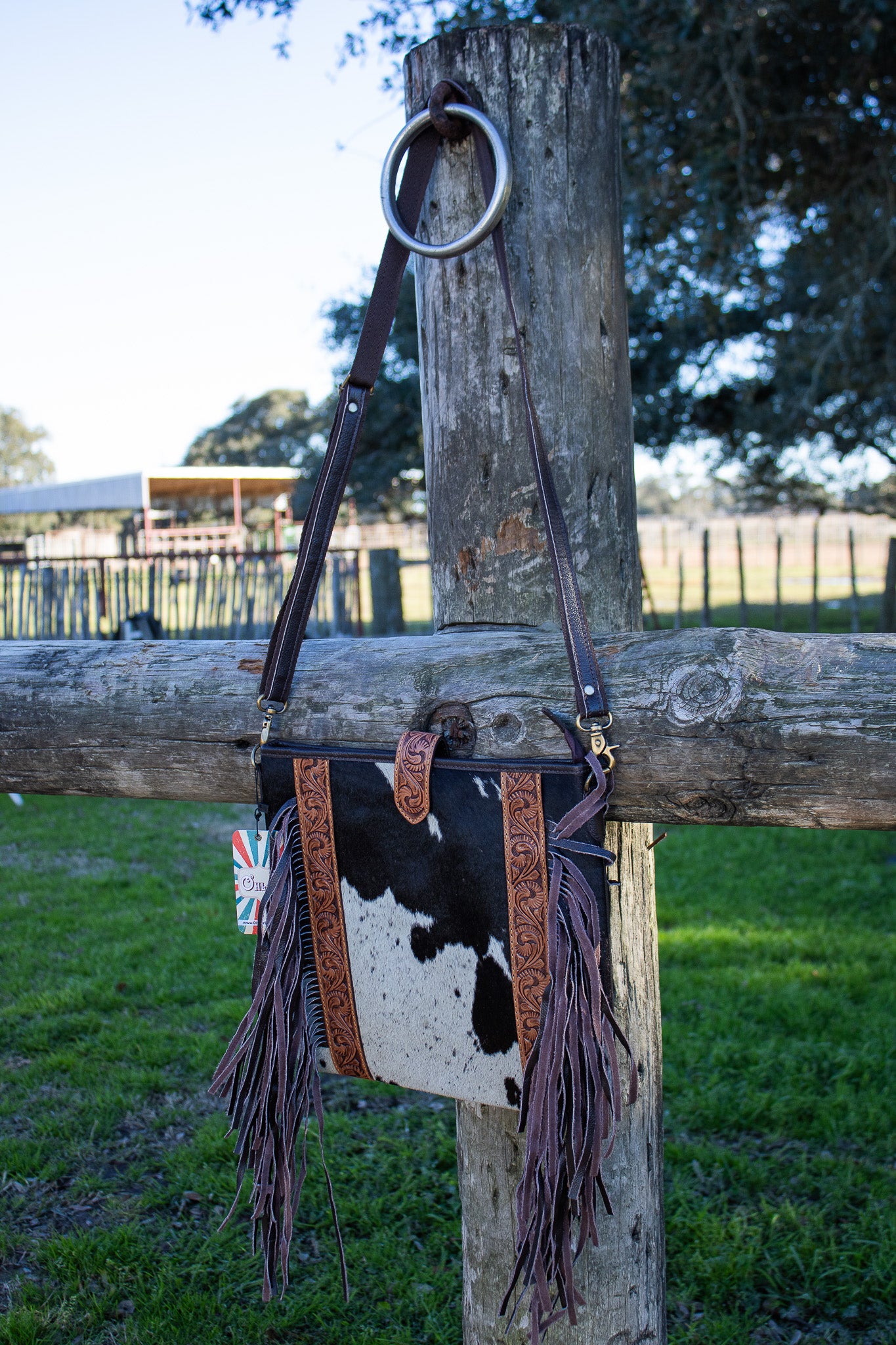 black and white cowhide purse hanging by brown shoulder strap with brown fringe and tooled leather