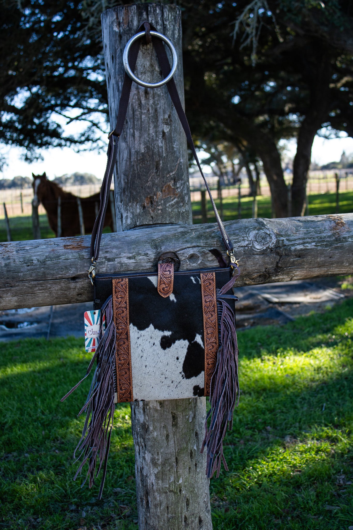 black and white cowhide purse 13x13" with a brown shoulder strap and fringe and hand tooled leather