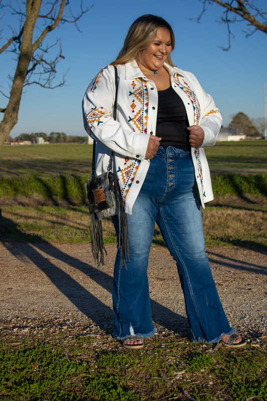 plus size model wearing a white denim jacket that has red, teal and yellow embroidery 